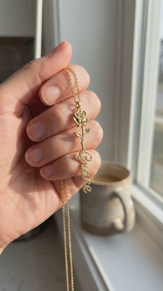 A hand holds the Birth Flower Name Necklace at a sunny kitchen window