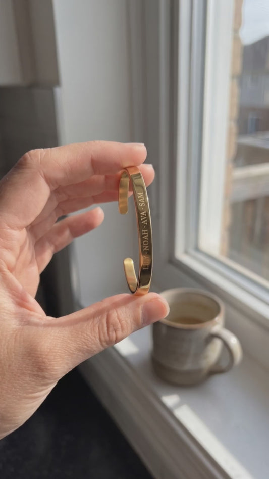 A hand holds the Grandma Cuff with the Grandkids' Names at a sunny kitchen window