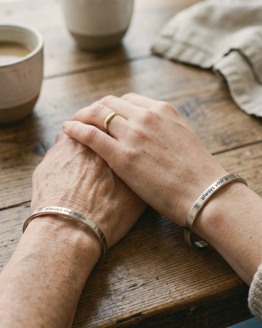 A mom and her grown daughter holding hands, each wearing an engraved cuff