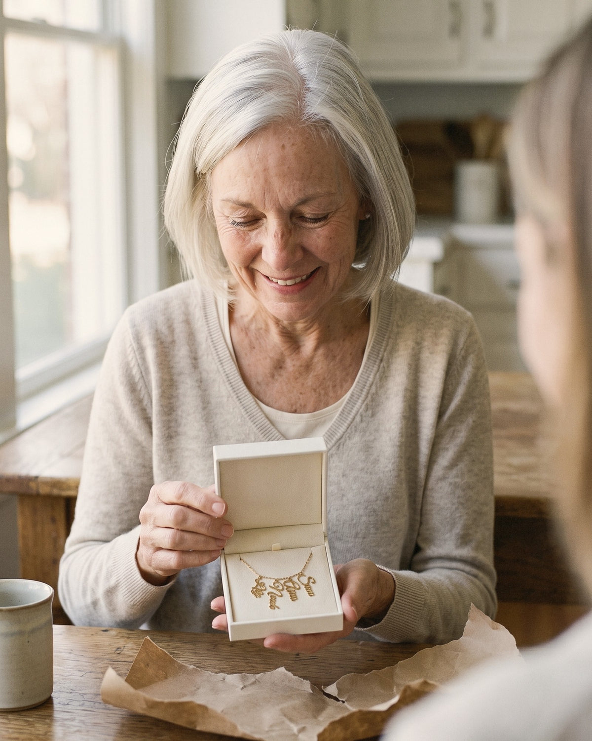 Grandmother opening a gift box holding her grandkids' names necklace at the kitchen table