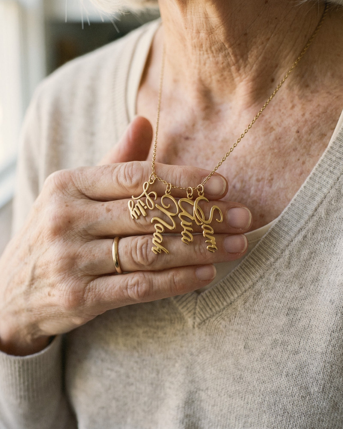 Close-up of a grandmother's hand holding four gold cursive name pendants