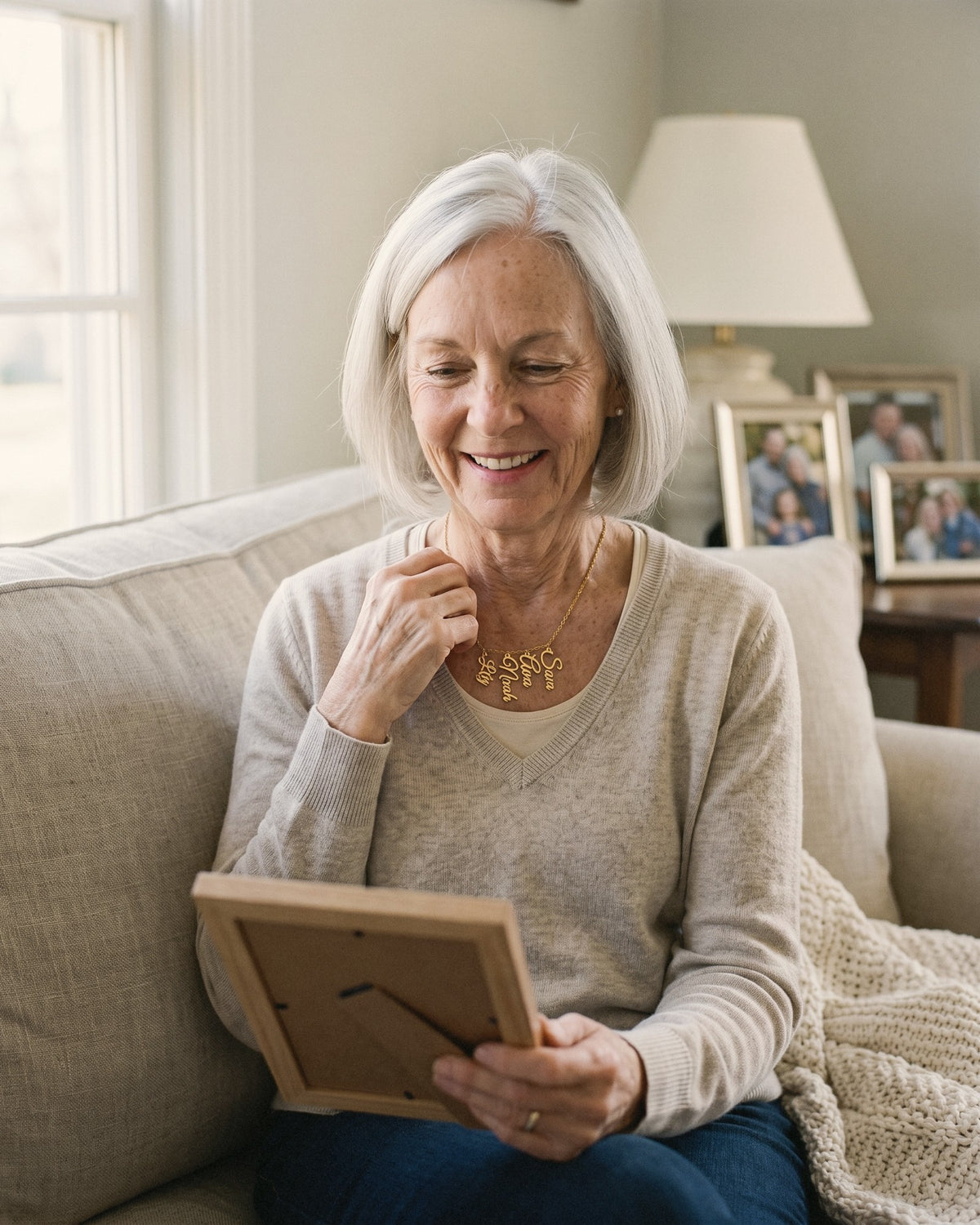 Grandmother on the sofa holding a picture frame and touching her grandkids' names necklace