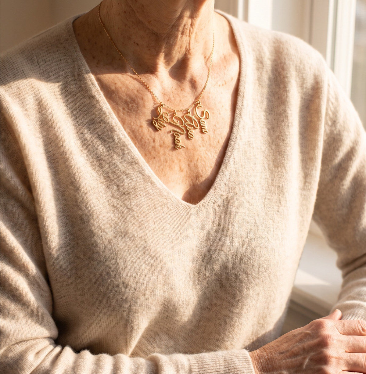 A woman in a cream sweater wearing a gold necklace with four grandkids' names: Lily, Noah, Ava and Sam