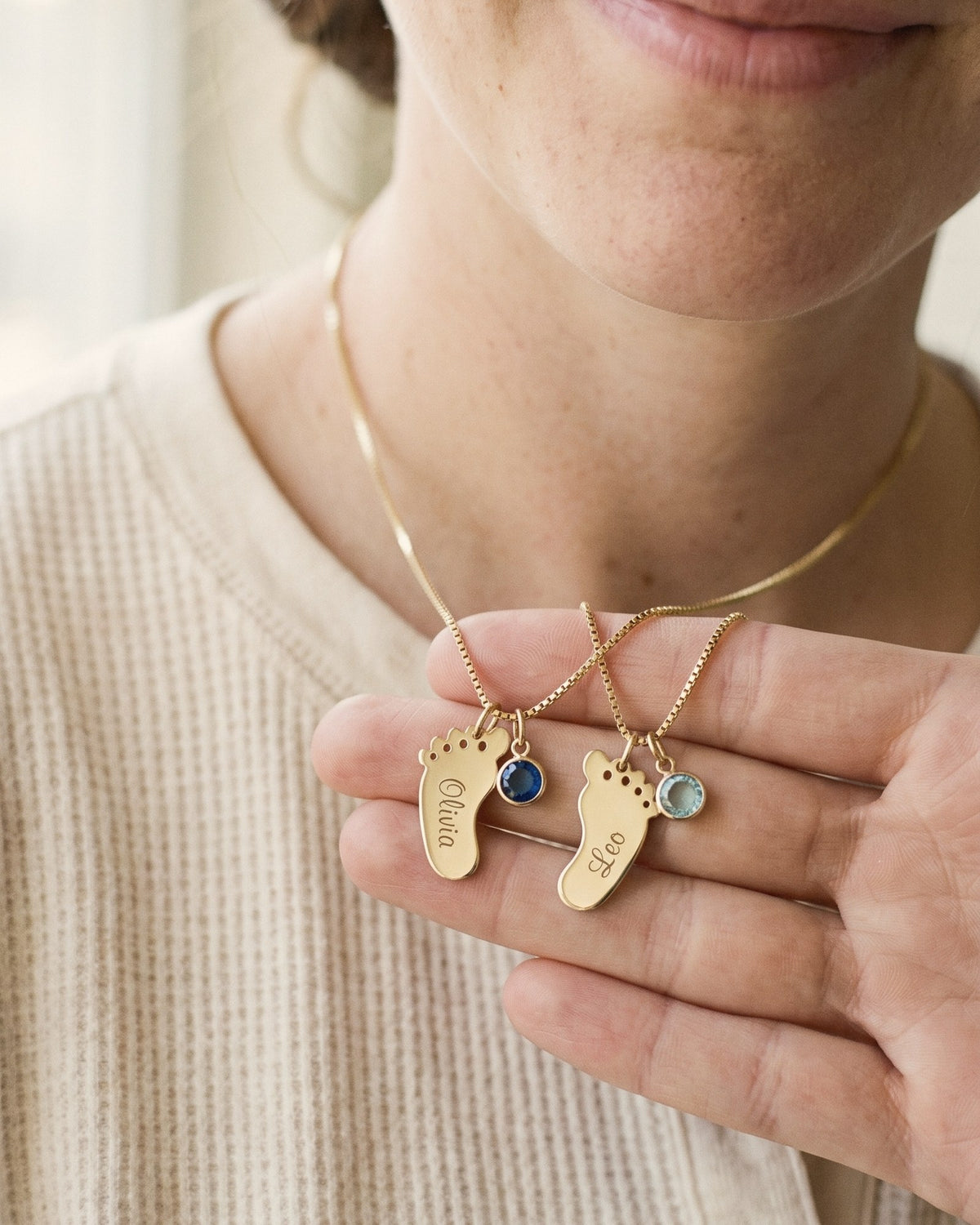 Close-up of two baby-feet charms engraved Olivia and Leo, each with its birthstone