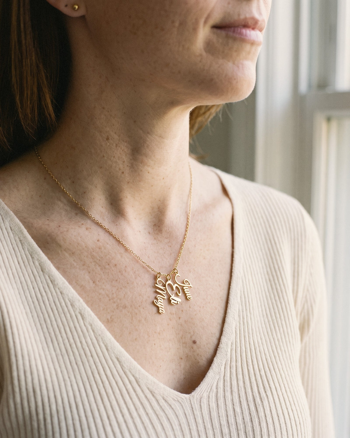 Mom wearing a gold necklace with her kids' names Maya, Eli and June hanging side by side