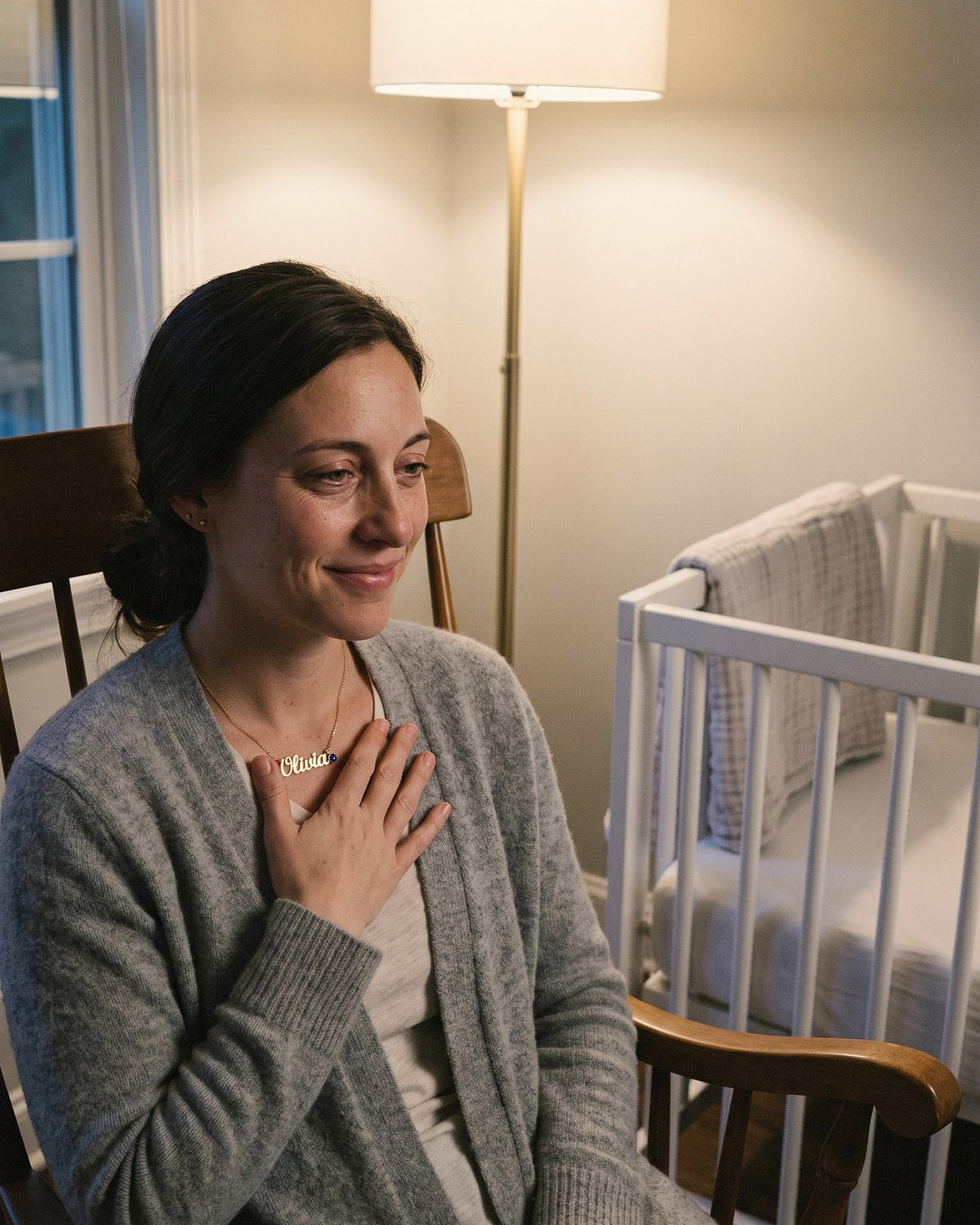 A new mom in a rocking chair in the nursery, her hand on her name necklace